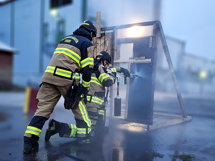 Två brandmän iklädda larmställ övar med skärmsläckare.